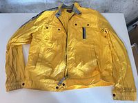 Front view of yellow ENRG jacket laid flat showing pockets, zipper, elastic cuffs and waistband