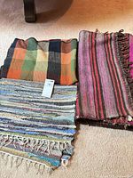 Three folded woven rugs showing plaid and two striped designs
