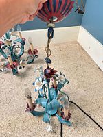 Close view of one chandelier showing turquoise frame, pink cups, white flowers and three candelabra sockets
