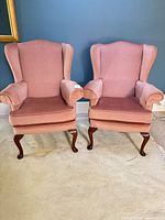 Front view of both pink wingback armchairs showing upholstery and cabriole legs