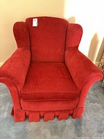 Front view of red wingback armchair showing overall design, arms, cushion, and skirted base