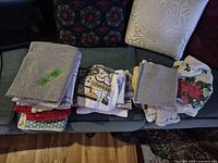 Stack of grey waffle weave towels, assorted coloured towels, printed and crocheted pieces on sofa