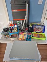 Overview of entire lot on table including Fiskars trimmer, calculator, storage cabinet, writing supplies and fasteners
