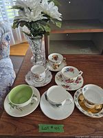 Five teacup and saucer sets arranged on table with clear glass vase behind