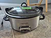 Front view of stainless Crock-Pot with glass lid, handles, power cord visible