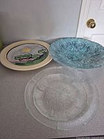 Three chargers visible: hand-painted ceramic, turquoise glass, clear glass