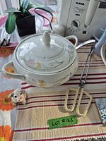 Deep fryer, covered serving dish, tongs, mixing utensil, placemat visible