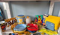 Shelf with assorted ceramic bowls, canisters, platter, mug, sign, napkins, decorative plaque and vase