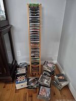 Tall wood CD rack filled with discs, additional CDs stacked on floor