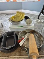 All items grouped on floor including bowls, pans, rolling pin, utensils, timer, jar, container