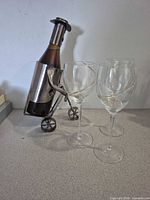 Metal wine bottle holder with decorative bottle and three gold-trim glasses