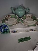 Group shot of mint teapot, two bowls on saucers, glass paperweight, souvenir tray