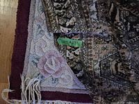 Corner of floral rug under folded oriental rug, showing fringe and pattern