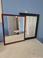 Both mirrors standing side by side on table, brown frame left, black frame right