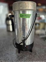 Full view of coffee urn showing stainless body, black base, handles and tap