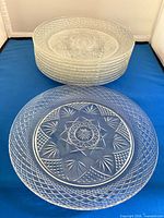 Stack of clear pressed glass plates with one plate displayed to show diamond lattice rim and starburst center