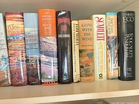 Row of hardcovers featuring Jean M. Auel series, Gone With the Wind, Scarlett, Foucault’s Pendulum and others