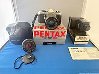 Full lot showing Pentax camera with mounted zoom lens, Nikon lens, Sunpak flash with box and manual, soft case, lens caps