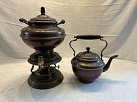 Full view of copper coffee urn on stand beside matching teapot