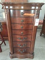 Front view of tall cherry jewelry armoire showing seven drawers and ornate pulls