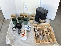 All items laid out: coffee maker, mugs, flatware tray, travel cup parts, SIGG tablets