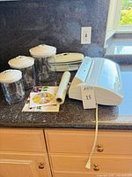 Vacuum sealer with power cord, three canisters, bag roll, manual and DVD on countertop