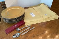 Stack of gold chargers, napkins, Gorham serving utensils and organza linen visible