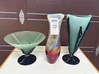 Front view of three glass pieces: green compote, multicolored vase, green vase with black vines
