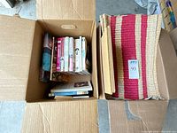 Two cartons showing cookbooks and folded woven runner plus straw placemats