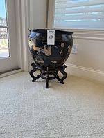 Front view of black and gold ceramic planter on wooden stand