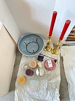Overhead view showing complete lot: bowl with stand, brass candlesticks with red tapers, assorted candles, candy dish, candle snuffer, glass holders, glass tile
