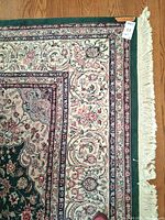 Corner of rug showing cream border, floral pattern, green edging, fringe