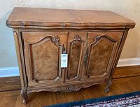 Front view showing paneled doors, carved apron, cabriole legs, light oak finish