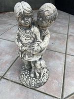 Full view of concrete boy and girl statue with dog on textured base