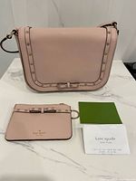 Front of blush pink Kate Spade handbag, card holder, authenticity cards on surface