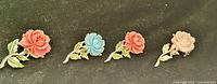 Four rose brooches lined up showing colour variety