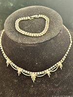 Necklace and bracelet displayed on black form for overall view