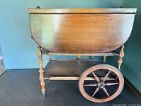 side view showing drop leaf, lower shelf, large wooden spoked wheel