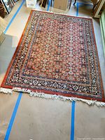 Full view of rust and navy Persian-style wool area rug with fringe
