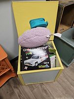 Open wooden storage box containing Ghostbusters building set, other boxed set, and plush pillow
