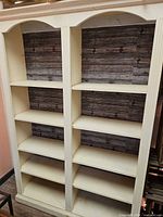 Front view of cream distressed two-column bookcase showing 10 shelves and rustic plank backing