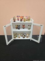 Front view of display cabinet open showing all Vinylmation figurines on shelves and top
