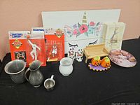 Group shot of all items on black table: plate, figures, books, pitchers, shakers, unicorn board
