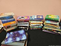 Three stacks of assorted paperback and hardcover books on table