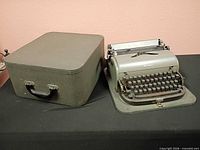 Typewriter seated in open carrying case beside closed case