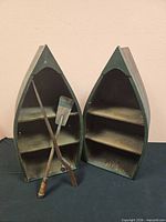 Pair of boat-shaped shelves standing upright with two oars leaning