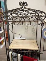 Front view showing metal frame, scroll top, hanging glass rack with glasses, wood shelf