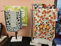 Assorted textiles on two metal racks: ivy runner, patchwork quilts, terry cloth towel