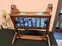 Cradle holding blue crochet blanket with decorative sign, frame, butterflies and dried stems visible behind