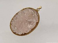 Front view of carved rose quartz pendant showing floral carving and gold-tone bezel
